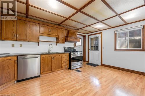 Kitchen featuring wood cabinetry, stainless steel appliances, a double basin sink with gooseneck faucet, light wood-finish flooring, and a coffered ceiling - 168 Britannia Avenue, Hamilton, ON - Indoor Photo Showing Kitchen