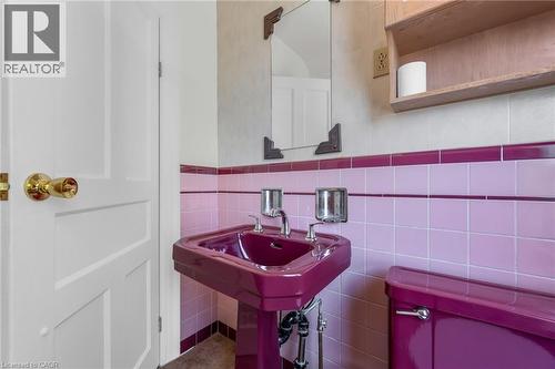 Pedestal sink with coordinating toilet, pink and purple tiled walls, polished brass hardware, and an overhead wooden shelf - 168 Britannia Avenue, Hamilton, ON - Indoor
