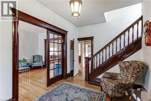 Grand entry hall with a dark wood staircase featuring turned balusters, light wood-finish flooring, and a glass-paneled pocket door - 18 Fairleigh Crescent, Hamilton, ON - Indoor Photo Showing Other Room