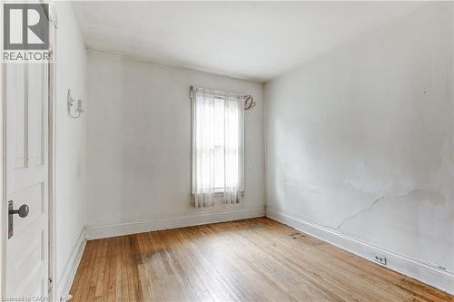 Hardwood flooring with baseboard trim, a single window with sheer curtains, and a white paneled door with a dark knob - 18 Fairleigh Crescent, Hamilton, ON - Indoor Photo Showing Other Room