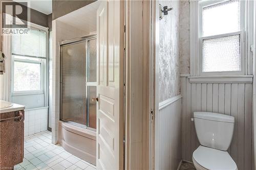 Bathroom featuring a white tile floor, a window with blinds, a shower-over-tub with a sliding glass door, a wood-finish vanity with a white countertop, and white beadboard paneling - 18 Fairleigh Crescent, Hamilton, ON - Indoor Photo Showing Bathroom