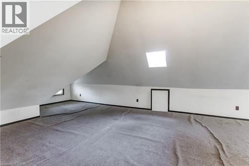 Sloped ceiling interior space featuring a skylight, gray carpeting, a built-in access panel, and a small window - 18 Fairleigh Crescent, Hamilton, ON - Indoor Photo Showing Other Room
