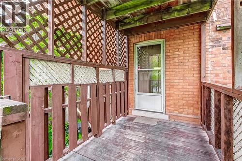 Covered wood-finish porch featuring a white screen door, brick exterior wall, wood railing, and decorative lattice panels - 18 Fairleigh Crescent, Hamilton, ON - Outdoor With Exterior