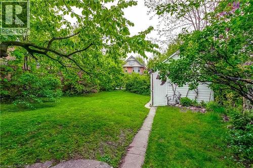 Expansive lawn area bordered by mature trees and shrubs, featuring a concrete walkway leading to a detached storage structure - 18 Fairleigh Crescent, Hamilton, ON - Outdoor