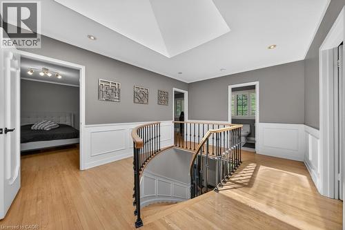 Hardwood flooring extends throughout this upper-level landing, featuring a graceful curved staircase with a dark iron and wood-finish railing - 25 Braemar Place, Hamilton, ON - Indoor