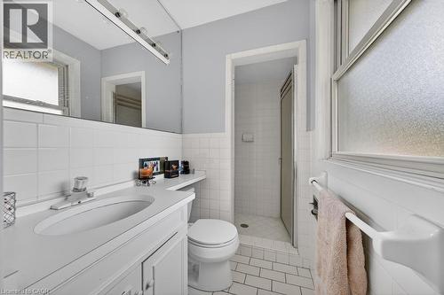Bathroom featuring a single vanity with integrated sink, white tile flooring, white wall tiling, a frosted window, and a shower with a sliding glass door - 25 Braemar Place, Hamilton, ON - Indoor Photo Showing Bathroom