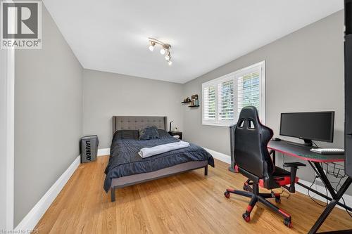 Bedroom featuring wood-finish flooring, light gray walls, a window with white louvered shutters, white baseboards, and a track light fixture - 25 Braemar Place, Hamilton, ON - Indoor Photo Showing Bedroom