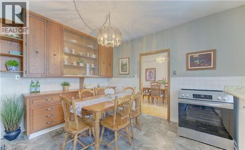 Eat-in kitchen featuring wood cabinetry with glass-front uppers, a built-in stainless steel range, light-toned tiled backsplash, and stone-look flooring - 1463 Kossuth Road, Cambridge, ON - Indoor Photo Showing Dining Room