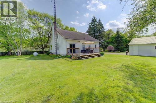 Spacious rear yard featuring an elevated wood-finish deck, white siding dwelling, separate utility building with metal roofing, mature trees, and a substantial grass area - 1463 Kossuth Road, Cambridge, ON - Outdoor