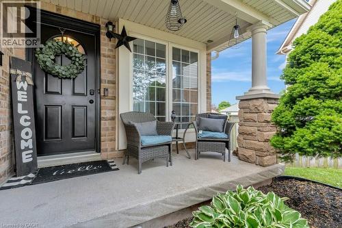 Brick facade with a covered porch featuring a decorative stone base column, a panel-style entry door, and large casement windows - 49 Small Court, Cambridge, ON - Outdoor With Deck Patio Veranda