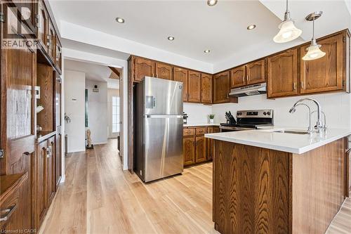 Kitchen featuring wood-finish cabinetry, stainless steel appliances, a white subway tile backsplash, and a central island with a white countertop and double basin sink - 488 Heather Hill Place, Waterloo, ON - Indoor Photo Showing Kitchen