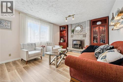 Spacious living area featuring light wood-finish flooring, a prominent brick-clad fireplace with a metal insert, and built-in wood cabinetry with glass display doors - 488 Heather Hill Place, Waterloo, ON - Indoor Photo Showing Living Room With Fireplace
