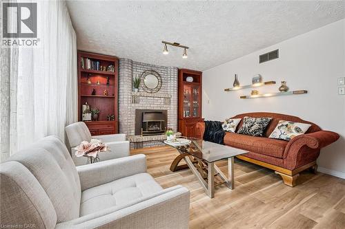 Living area featuring wood-finish flooring, a brick fireplace with a built-in firebox, a built-in corner bookcase, an additional built-in cabinet with glass doors, and wall-mounted display shelves - 488 Heather Hill Place, Waterloo, ON - Indoor Photo Showing Living Room With Fireplace