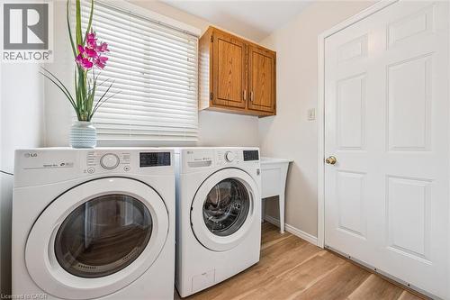 Dedicated laundry space featuring wood-finish flooring, white paneled door, and upper cabinetry - 488 Heather Hill Place, Waterloo, ON - Indoor Photo Showing Laundry Room
