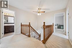 Upper-level landing featuring light-toned carpeting, a traditional wood-finish banister, and a ceiling fan with integrated lighting - 