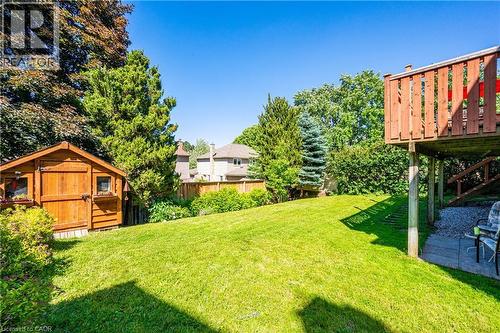 Expansive backyard featuring a lush green lawn, mature trees, a wood storage shed, and a raised wood deck with privacy railing - 488 Heather Hill Place, Waterloo, ON - Outdoor With Deck Patio Veranda