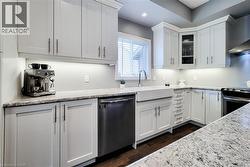 Modern kitchen featuring white cabinetry, light-toned countertops, a farmhouse sink, stainless steel appliances, and dark wood-finish flooring - 