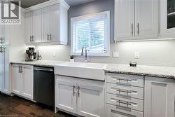 Kitchen featuring white shaker-style cabinetry, granite countertops, and a white farmhouse sink - 