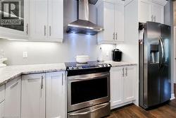 Modern kitchen featuring white shaker cabinetry, stainless steel appliances, granite countertops, and wood-finish flooring - 