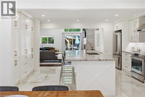Bright kitchen featuring white shaker cabinetry, stainless steel appliances, a large center island with a sink, and marble-look flooring - 24 Glenwood Crescent, Hamilton, ON - Indoor Photo Showing Kitchen