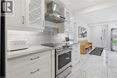 White cabinetry with glass-front accents, stainless steel appliances, marble-look countertops, matching backsplash, and marble-look flooring - 24 Glenwood Crescent, Hamilton, ON - Indoor Photo Showing Kitchen