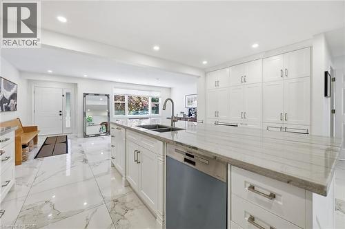 Bright kitchen featuring extensive white cabinetry with brushed nickel hardware, a large central island with a sink and integrated dishwasher, and a stone countertop - 24 Glenwood Crescent, Hamilton, ON - Indoor Photo Showing Kitchen With Double Sink