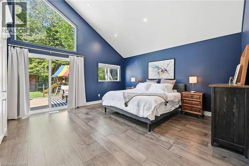 Vaulted ceiling bedroom featuring wood-finish flooring, a full wall of custom built-in cabinetry, and a large sliding glass door with an oversized triangular window above - 24 Glenwood Crescent, Hamilton, ON - Indoor Photo Showing Bedroom
