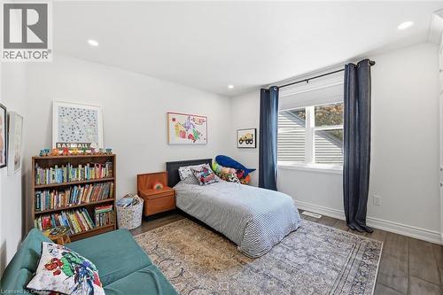 Bright interior space featuring recessed lighting, dark wood-finish flooring, white baseboards, and a window with white blinds and dark blue curtains - 24 Glenwood Crescent, Hamilton, ON - Indoor Photo Showing Bedroom
