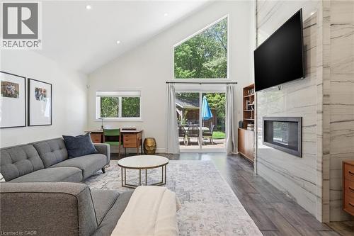 Vaulted ceiling living area featuring wood-finish flooring, a contemporary fireplace with a stone surround, and abundant natural light from multiple windows, including a large triangular window - 24 Glenwood Crescent, Hamilton, ON - Indoor Photo Showing Living Room With Fireplace