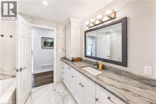 Bathroom featuring an extended vanity with dual sinks, a stone countertop, white shaker-style cabinetry, and large format marble-look tile flooring - 24 Glenwood Crescent, Hamilton, ON - Indoor Photo Showing Bathroom