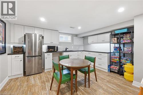 Bright kitchen area featuring white shaker-style cabinetry, dark countertops, a stainless steel refrigerator, and wood-finish flooring - 24 Glenwood Crescent, Hamilton, ON - Indoor Photo Showing Kitchen