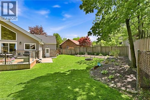 Expansive backyard featuring a wood-finish deck with glass panel railing, a stone patio, a large lawn, and a landscaped garden bed - 24 Glenwood Crescent, Hamilton, ON - Outdoor With Backyard