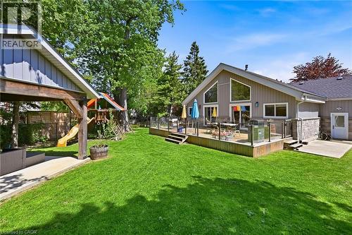 Spacious green lawn featuring a multi-level deck with glass panel railing, a covered patio area, and mature trees providing natural shade - 24 Glenwood Crescent, Hamilton, ON - Outdoor With Deck Patio Veranda