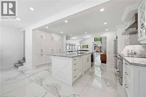 Open-concept kitchen featuring extensive white cabinetry, large center island with integrated sink, stainless steel appliances, and marble-look flooring - 24 Glenwood Crescent, Hamilton, ON - Indoor Photo Showing Kitchen With Upgraded Kitchen