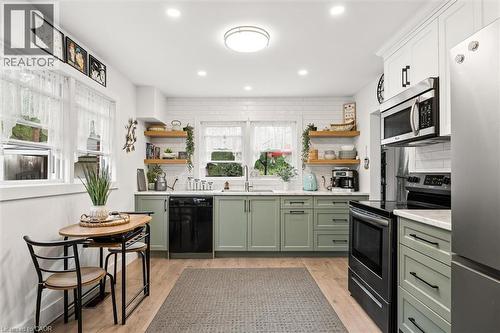 Kitchen featuring light green base cabinetry, white upper cabinetry, subway tile backsplash, stainless steel appliances, and wood-finish flooring - 786 S Stirling Avenue S, Kitchener, ON - Indoor Photo Showing Kitchen