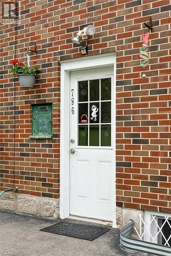 Brick exterior featuring a white paneled door with divided lite window, security lighting, and a green mail slot - 786 S Stirling Avenue S, Kitchener, ON - Outdoor With Exterior