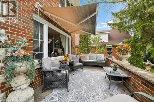 Brick patio featuring a retractable awning, stone-capped brick retaining wall, and a patterned outdoor rug - 786 S Stirling Avenue S, Kitchener, ON - Outdoor With Deck Patio Veranda With Exterior