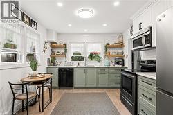 Kitchen featuring light green base cabinetry, white upper cabinetry, subway tile backsplash, stainless steel appliances, and wood-finish flooring - 