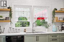 Kitchen featuring a dual-basin stainless steel sink with a gooseneck faucet, light green cabinetry with dark hardware, and a white subway tile backsplash - 