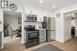 Modern kitchen featuring white shaker cabinetry, stainless steel appliances including a microwave, range, and refrigerator, light wood-finish flooring, and a subway tile backsplash - 