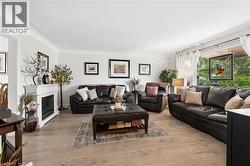Bright living space featuring wood-finish flooring, a white mantel fireplace, crown molding, and abundant natural light from a large window - 