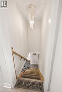 Modern spiral chandelier illuminating a staircase with wood-finish treads, black wrought iron balusters, and a natural wood handrail - 