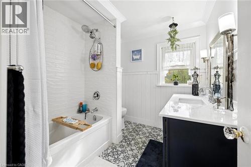 Bathroom featuring a white subway tile shower surround, a white bathtub with chrome fixtures, a dark wood vanity with a white countertop and undermount sink, and patterned floor tiling - 786 S Stirling Avenue S, Kitchener, ON - Indoor Photo Showing Bathroom