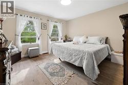 Bedroom featuring two double-hung windows, light-toned walls, and wood-finish flooring - 