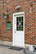 Brick exterior featuring a white paneled door with divided lite window, security lighting, and a green mail slot - 