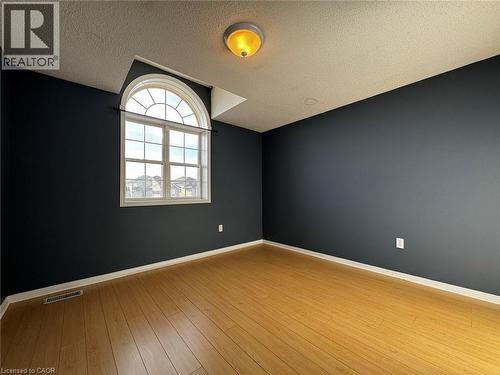 Room featuring a prominent arched window, wood-finish flooring, dark-painted walls, and white baseboards - 37 Northcliffe Crescent, Cambridge, ON - Indoor Photo Showing Other Room