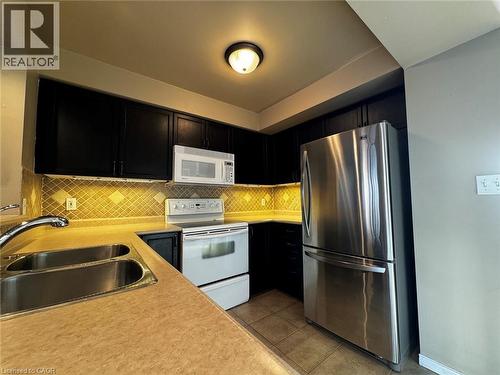 Well-appointed kitchen featuring dark cabinetry, a double basin stainless steel sink, and a stainless steel refrigerator - 37 Northcliffe Crescent, Cambridge, ON - Indoor Photo Showing Kitchen With Double Sink