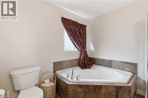 White built-in corner soaking tub with tiled surround, adjacent to a white toilet with a standard flush - 84 Duncairn Crescent, Hamilton, ON - Indoor Photo Showing Bathroom