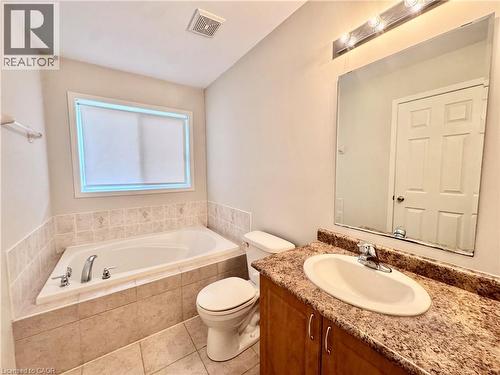 Bathroom featuring a built-in tub with tile surround, a single vanity with wood-finish cabinetry, an oval undermount sink, and a stone-look countertop - 110 Highland Road E Unit# 53, Kitchener, ON - Indoor Photo Showing Bathroom