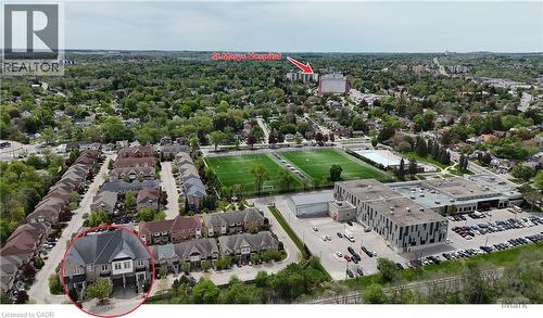 Aerial perspective showcasing a residential street with attached townhomes, positioned near a large institutional building with an expansive parking lot, and adjacent to athletic fields - 110 Highland Road E Unit# 53, Kitchener, ON - Outdoor With View